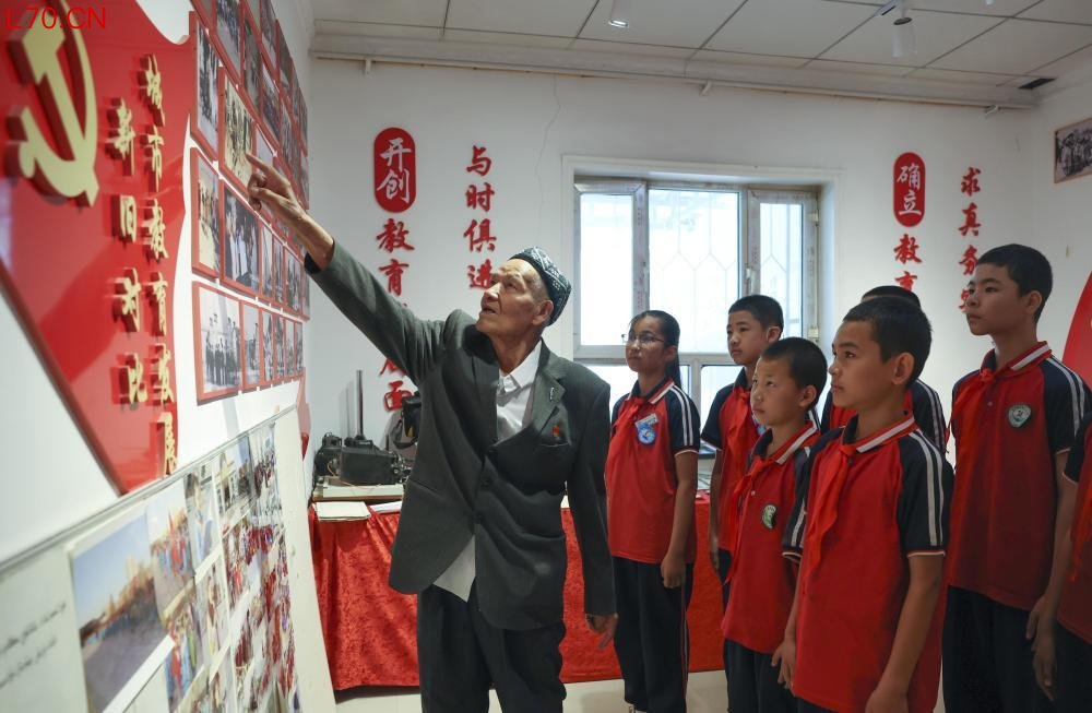 2026年6月24日,在位于新疆库尔勒市恰尔巴格乡萨依巴格村的“梨城记忆”文化小院,克热木·木沙(左)在为前来参观的学生们讲述老照片背后的故事。新华社记者 王菲 摄